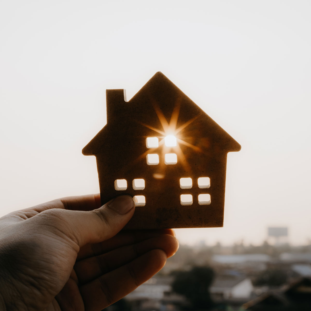 Hand holding house cutout with sun shining through